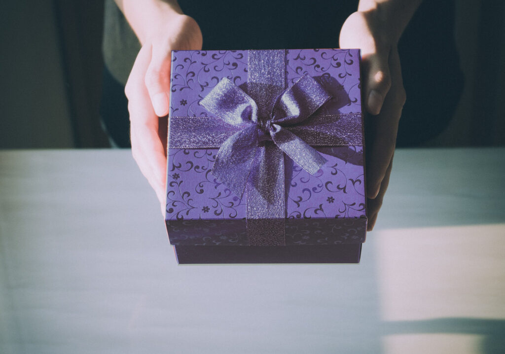 Sur la photo, deux mains tiennent une boîte cadeau bleue, ornée d'un ruban de la même couleur.
