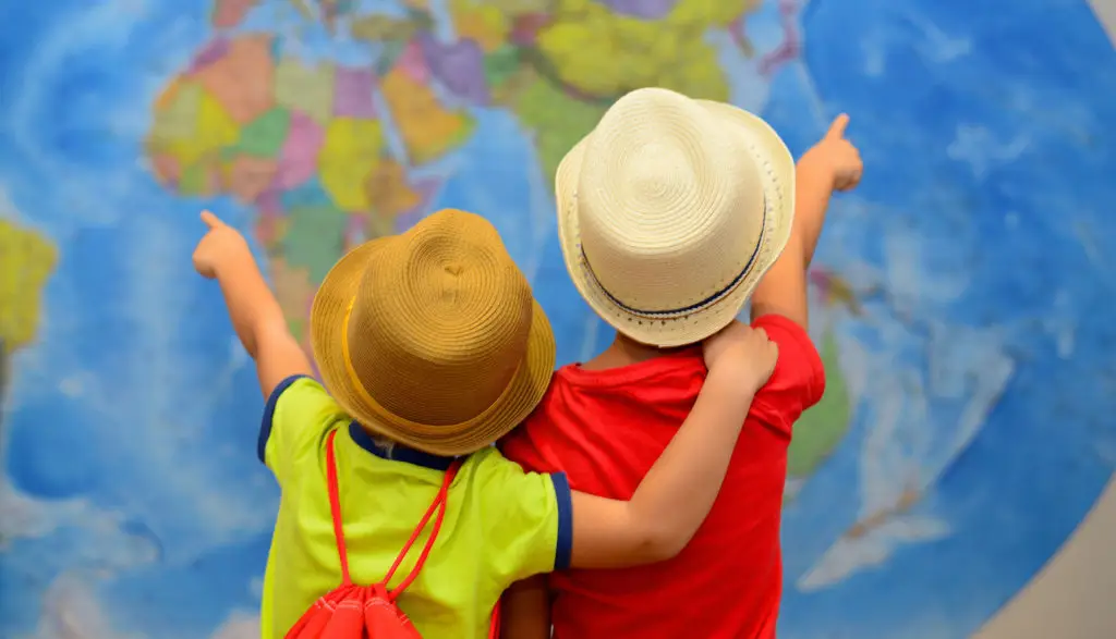 Nell'immagine due bambini di spalle, che si abbracciano mentre osservano l'immagine di un grosso mappamondo